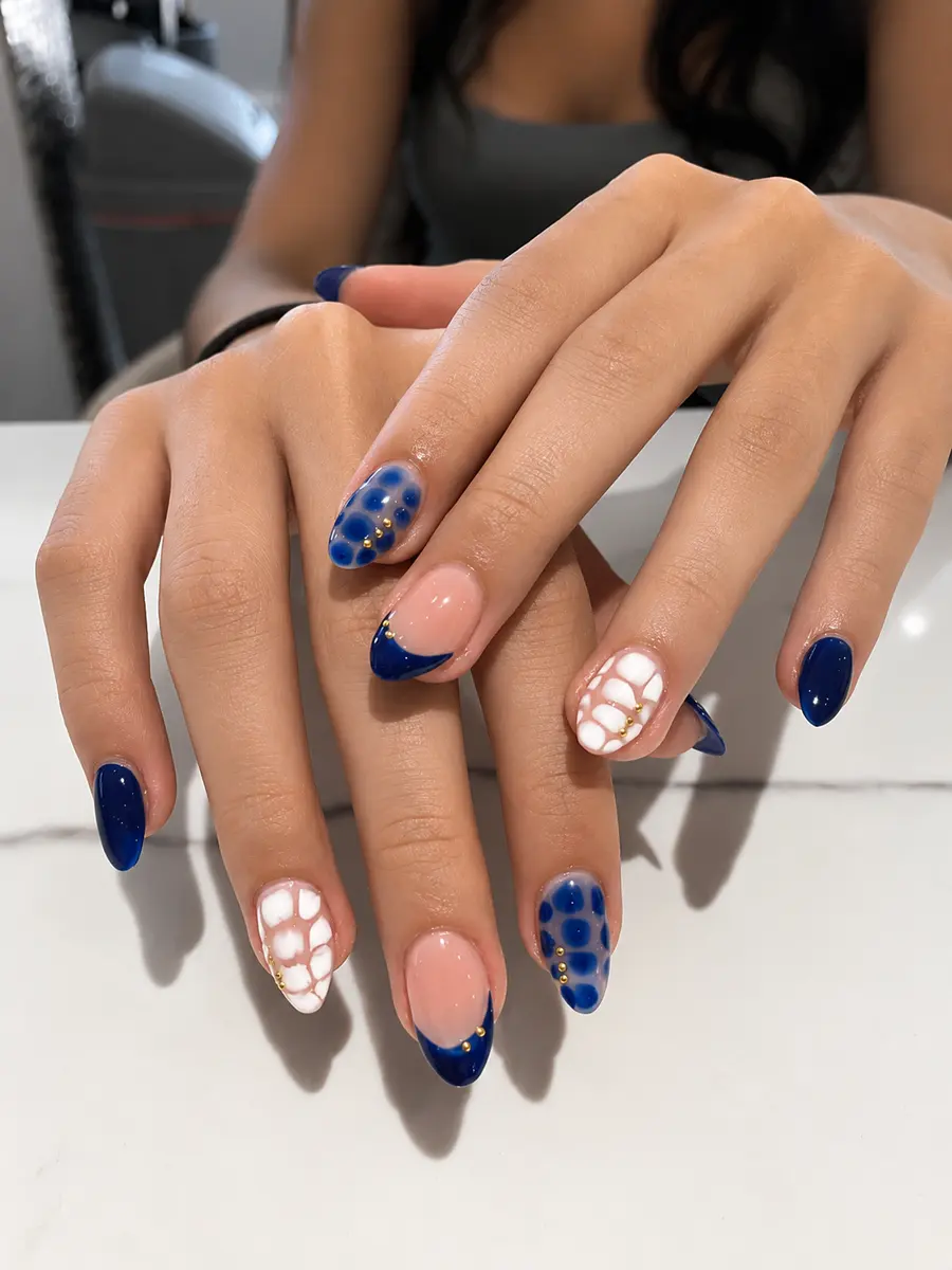 Navy blue nail art with a white lace pattern and gold studs